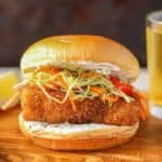Delicious crispy fish fillet sandwich topped with fresh shredded vegetables and creamy sauce in a so.