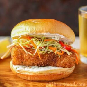 Delicious crispy fish fillet sandwich topped with fresh shredded vegetables and creamy sauce in a so.